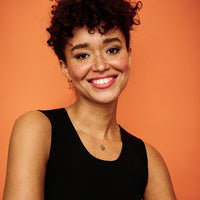 Model wearing gold vermeil Toolally mood huggie earring against an orange backdrop